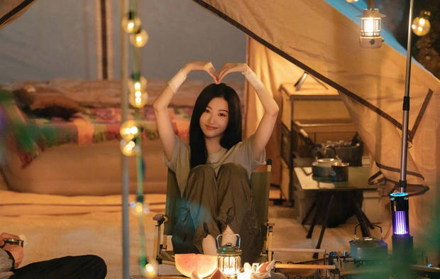 景甜坐在帐篷旁对着镜头比心，十分甜美迷人。